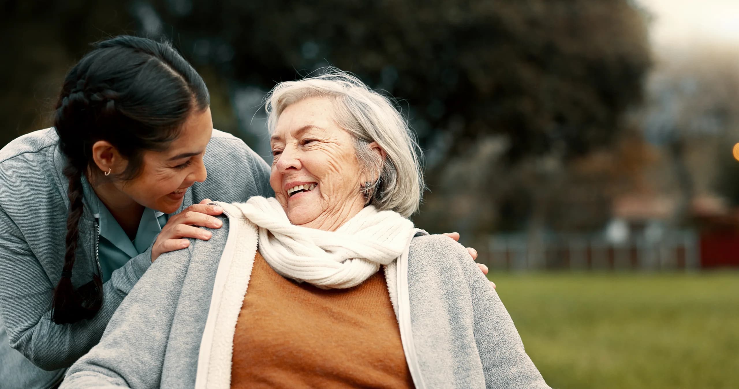 Betreuerin und Seniorin lachen gemeinsam im Garten