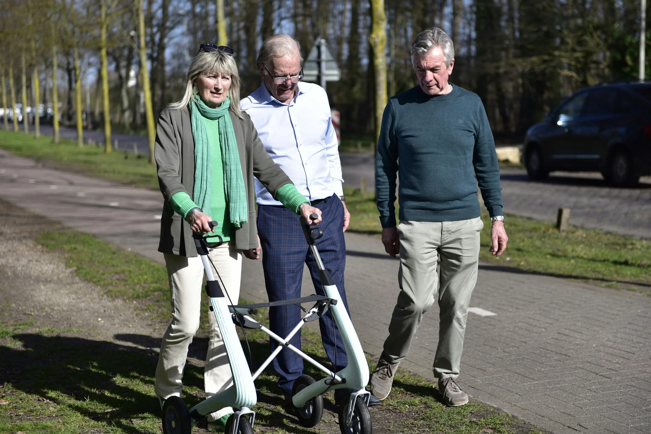 Seniorin mit Rollator geht mit zwei Begleitern spazieren